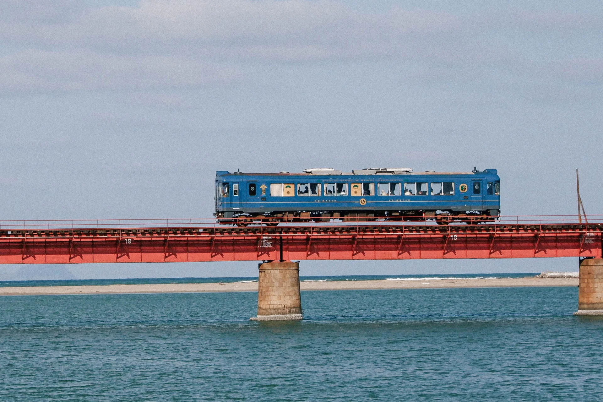 Blue train crossing a red bridge over water